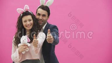 年轻夫妇站在粉红色的背景上。 在这个节目中，一个手势课微笑着，手里拿着一个柔软的玩具